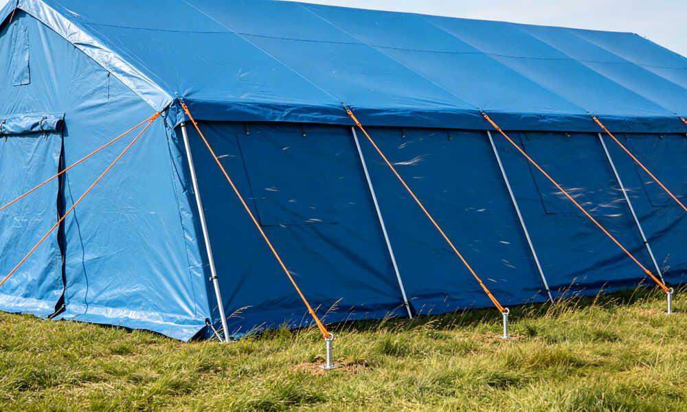 Emergency frame tent secured with thick guy ropes and steel ground stakes in windy field conditions