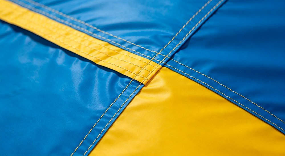 Closeup of inflatable tent fabric showing reinforced stitching and heat welded seams in blue and yellow material during factory quality inspection