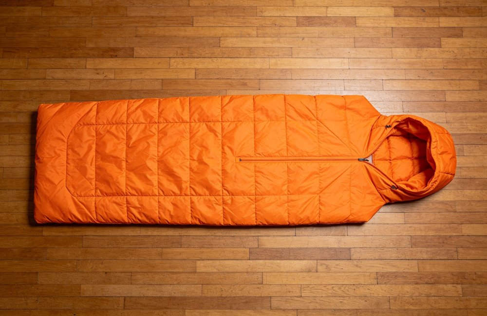 Top view flat lay of blue and green envelope sleeping bags laid horizontally side by side for dimension comparison on clean white background, showing size differences, product catalog style, no people