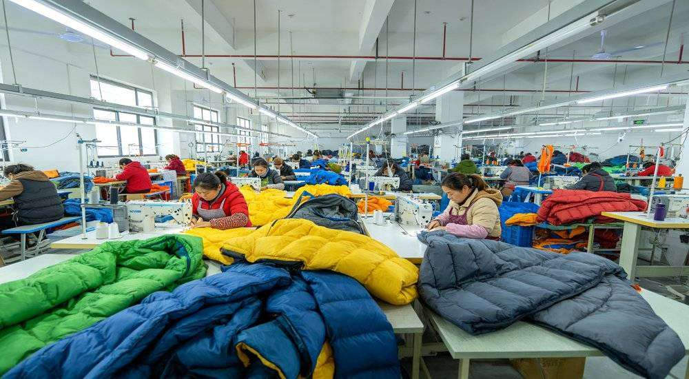Wide angle view of sleeping bag manufacturer factory comparison production line workers sewing colorful bags